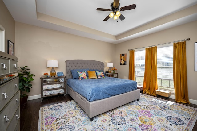 bedroom featuring a tray ceiling, dark wood-type flooring, and baseboards