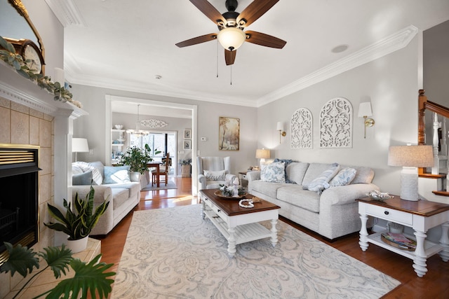 living area featuring ornamental molding, a tile fireplace, ceiling fan with notable chandelier, and wood finished floors