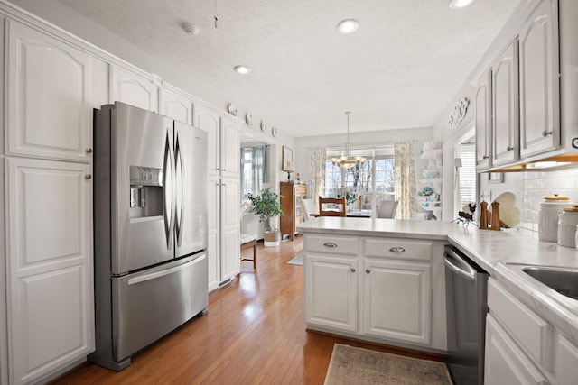 kitchen featuring appliances with stainless steel finishes, a peninsula, light wood-style floors, a notable chandelier, and white cabinetry