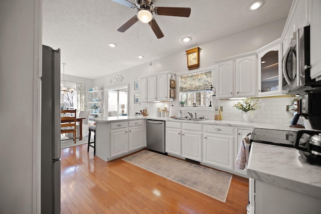 kitchen featuring light wood-type flooring, appliances with stainless steel finishes, a peninsula, white cabinets, and a sink