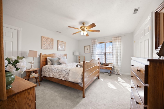 bedroom with light carpet, visible vents, a textured ceiling, and ceiling fan