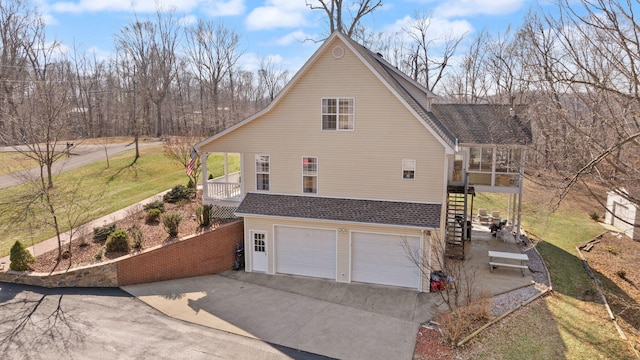 view of side of property featuring stairway, driveway, roof with shingles, an attached garage, and a lawn