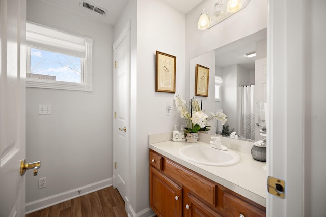 full bath with visible vents, vanity, baseboards, and wood finished floors