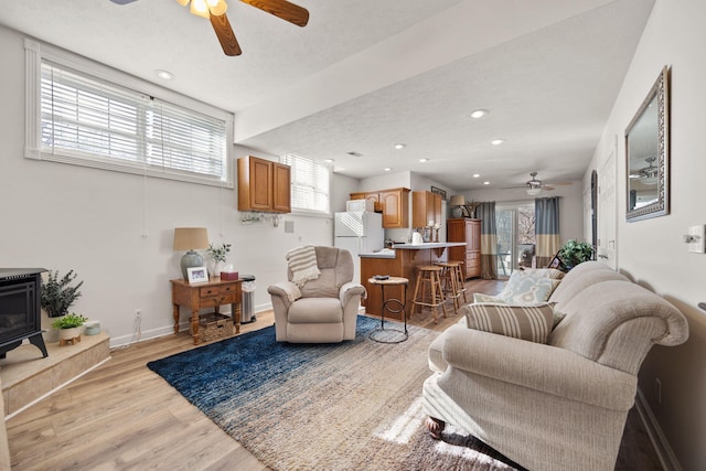 living room featuring baseboards, a healthy amount of sunlight, light wood-style flooring, and a wood stove