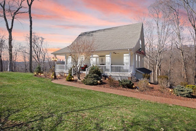 view of front of house with a porch, a ceiling fan, a front lawn, and roof with shingles