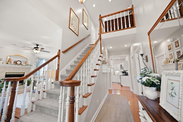 stairs featuring a ceiling fan, wood finished floors, recessed lighting, baseboards, and a towering ceiling