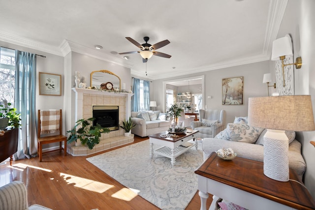 living room with ceiling fan, ornamental molding, wood finished floors, and a tile fireplace