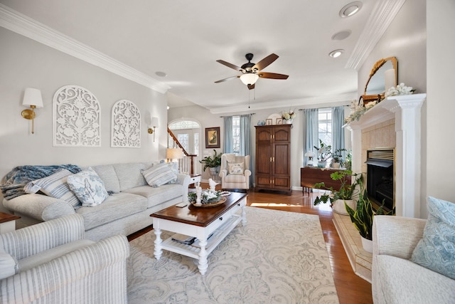 living area featuring crown molding, ceiling fan, stairway, a fireplace, and wood finished floors