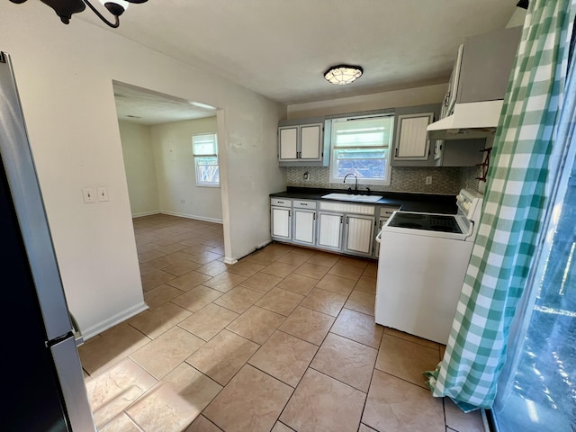 kitchen with tasteful backsplash, dark countertops, under cabinet range hood, white electric range oven, and a sink