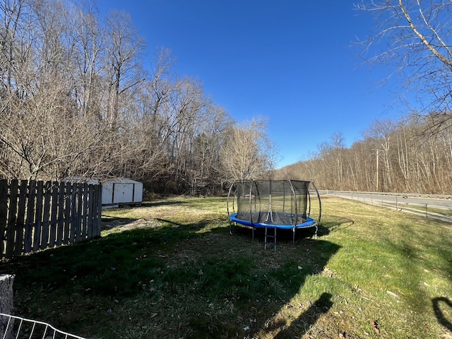 view of yard with an outdoor structure, a storage shed, a trampoline, and fence