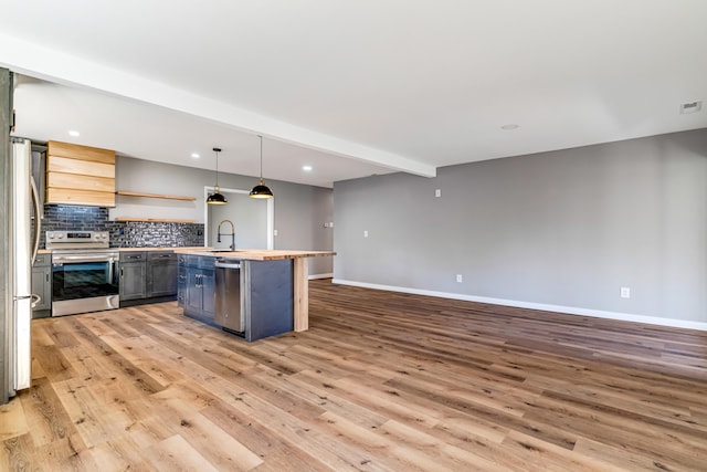 kitchen with beam ceiling, a center island with sink, appliances with stainless steel finishes, light wood finished floors, and decorative backsplash