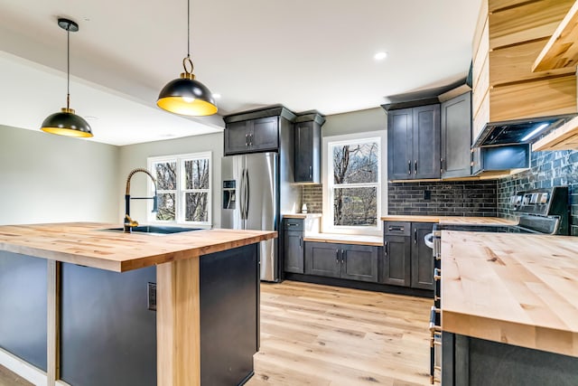 kitchen with light wood-style flooring, a sink, appliances with stainless steel finishes, wood counters, and tasteful backsplash