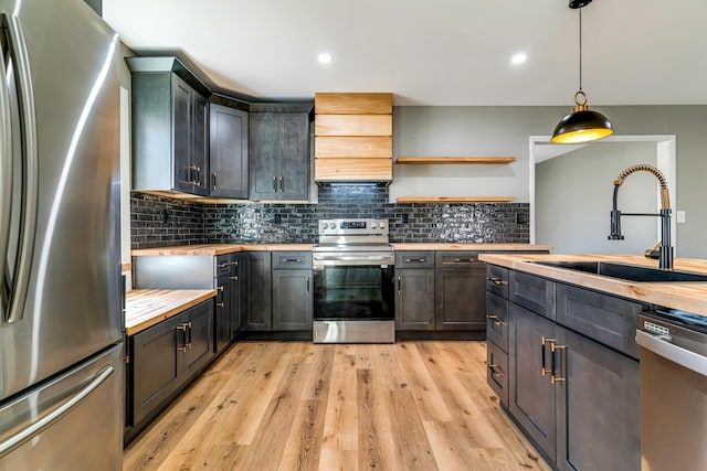 kitchen featuring tasteful backsplash, light wood finished floors, butcher block countertops, appliances with stainless steel finishes, and a sink