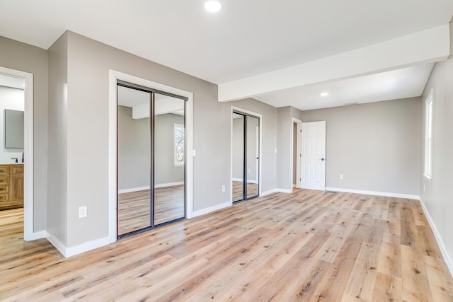 unfurnished bedroom featuring recessed lighting, baseboards, light wood-type flooring, and multiple closets