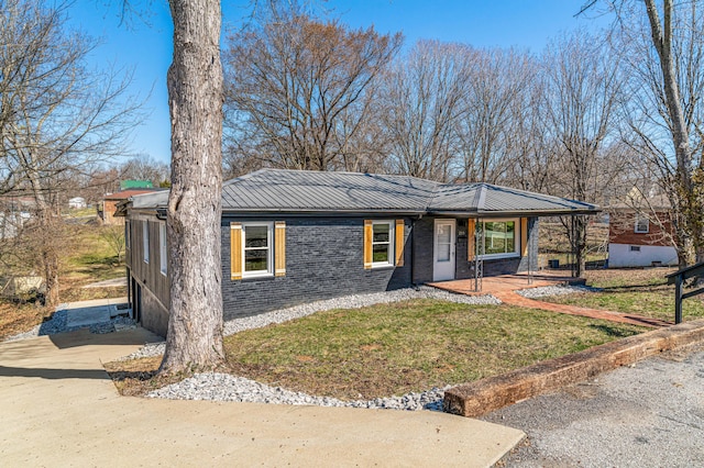 view of front of home featuring metal roof, a front yard, brick siding, and driveway