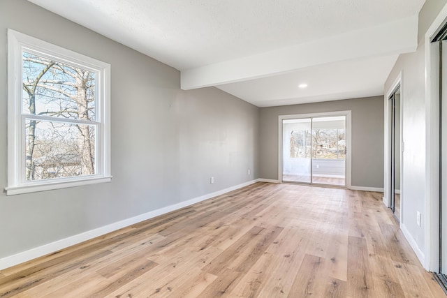 spare room featuring light wood finished floors, beamed ceiling, and baseboards