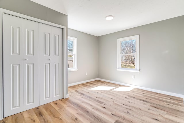 unfurnished bedroom featuring a closet, multiple windows, baseboards, and light wood finished floors