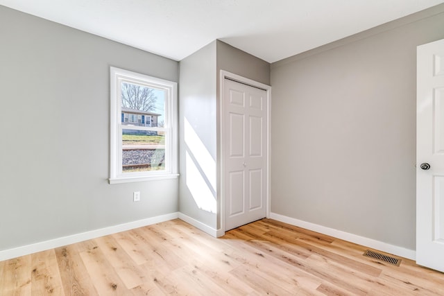 unfurnished bedroom with light wood finished floors, visible vents, a closet, and baseboards