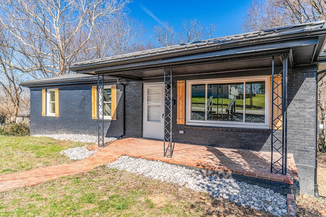 view of front of house featuring metal roof, brick siding, and a porch