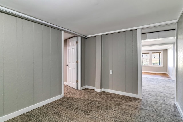 unfurnished bedroom with carpet flooring, baseboards, and wood walls