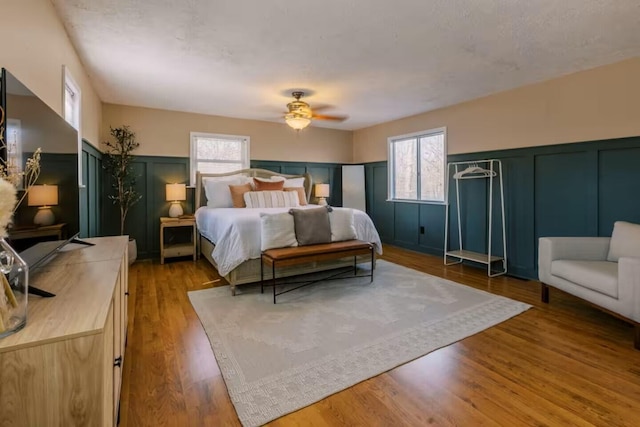 bedroom with a decorative wall, ceiling fan, a wainscoted wall, and wood finished floors