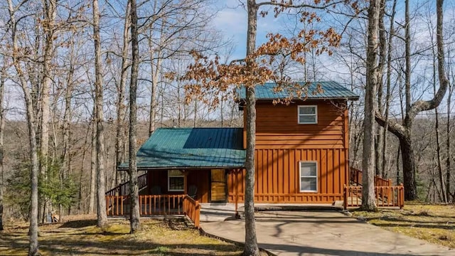 rustic home with board and batten siding, covered porch, driveway, and metal roof