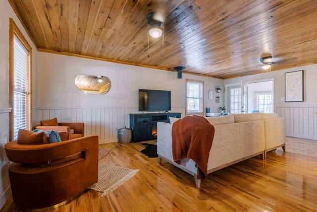 living room with light wood-style flooring, ornamental molding, ceiling fan, wainscoting, and wooden ceiling