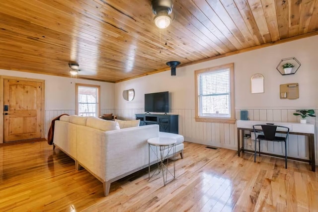 living room featuring light wood finished floors, a wainscoted wall, wood ceiling, and ceiling fan