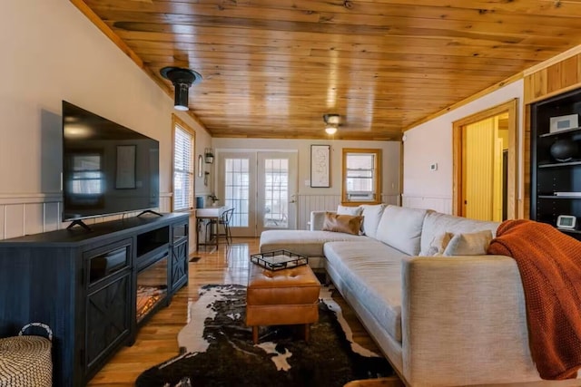 living area with wainscoting, wood ceiling, a wood stove, and light wood-style floors