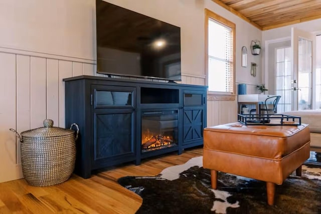 interior space featuring a glass covered fireplace, wood ceiling, wood finished floors, and a wainscoted wall