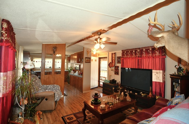 living area with a ceiling fan, vaulted ceiling with beams, and wood finished floors