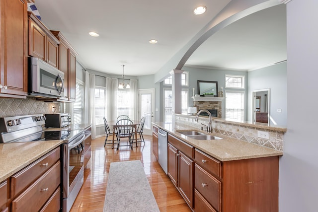 kitchen with brown cabinetry, arched walkways, a sink, appliances with stainless steel finishes, and backsplash