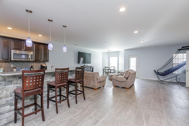 kitchen with a breakfast bar, stainless steel microwave, dark brown cabinetry, decorative backsplash, and hanging light fixtures