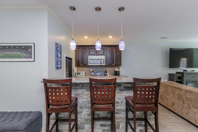 kitchen with stainless steel microwave, dark brown cabinets, a kitchen bar, and open floor plan