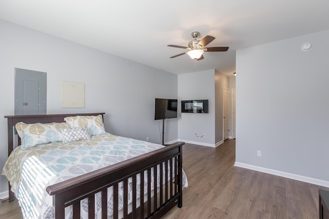 bedroom featuring a ceiling fan, electric panel, wood finished floors, and baseboards