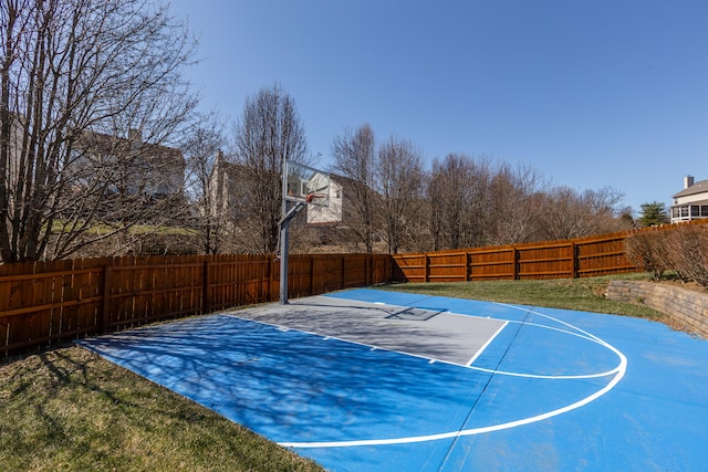 view of basketball court featuring a yard, basketball hoop, and a fenced backyard