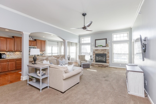 living area featuring light carpet, a stone fireplace, ceiling fan, and decorative columns