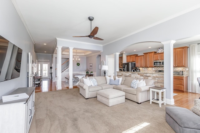 living room featuring ceiling fan with notable chandelier, arched walkways, crown molding, decorative columns, and light colored carpet