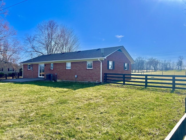 view of side of property featuring a yard, fence, brick siding, and central AC