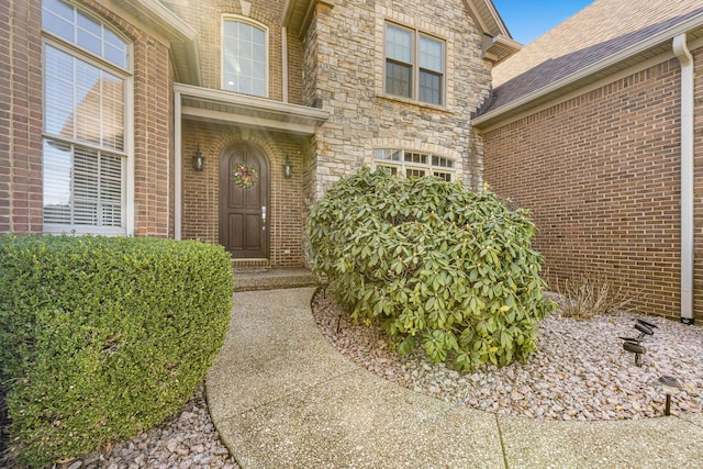 doorway to property featuring stone siding, brick siding, and a shingled roof