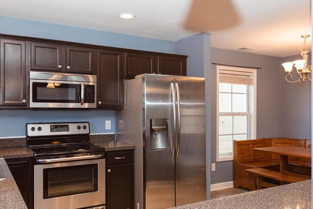 kitchen with dark stone countertops, baseboards, dark brown cabinetry, appliances with stainless steel finishes, and a chandelier