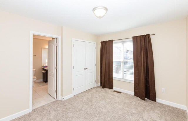 unfurnished bedroom featuring visible vents, baseboards, a closet, light colored carpet, and connected bathroom