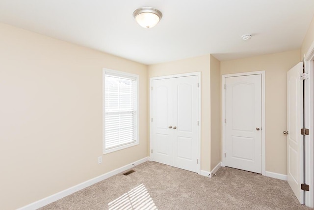 unfurnished bedroom featuring visible vents, baseboards, a closet, and light carpet