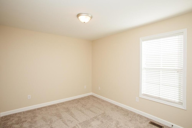 empty room with a wealth of natural light, visible vents, carpet, and baseboards