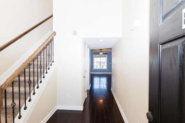 hallway with visible vents, baseboards, a high ceiling, and dark wood-style floors