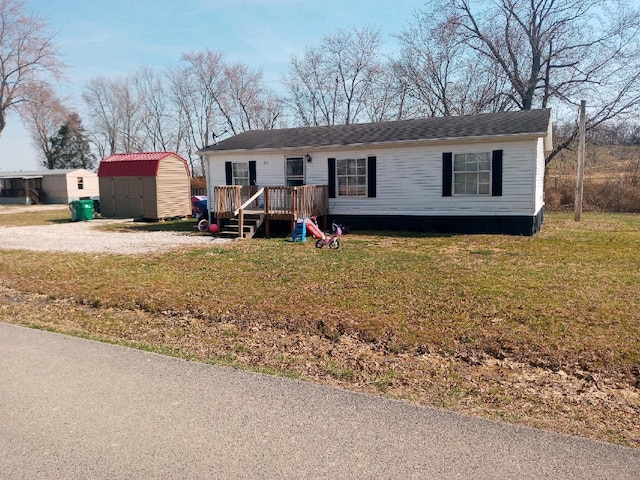 manufactured / mobile home with a wooden deck, an outdoor structure, a front lawn, and a shed