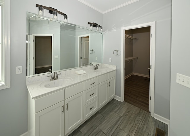 bathroom featuring a walk in closet, ornamental molding, a sink, double vanity, and baseboards