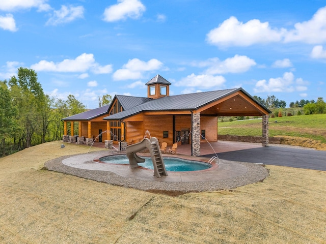 exterior space with faux log siding, an attached carport, a patio area, and an outdoor pool