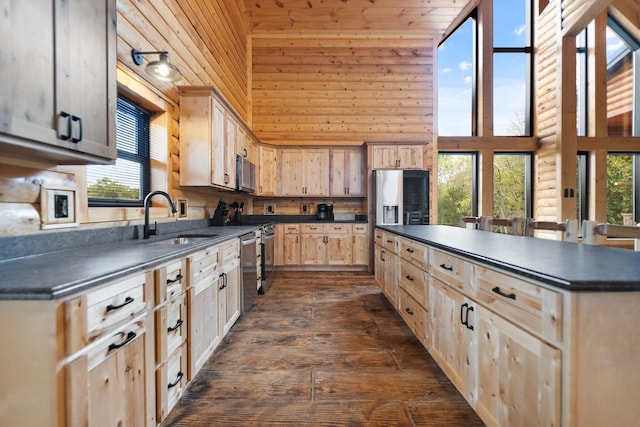 kitchen with a sink, dark countertops, appliances with stainless steel finishes, and light brown cabinets