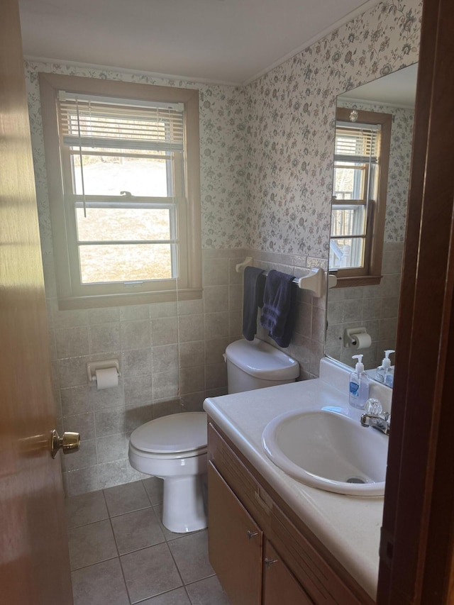 half bath with toilet, wallpapered walls, tile walls, wainscoting, and tile patterned flooring